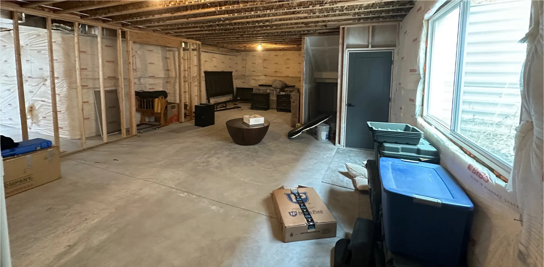 Before — basement finishing in Utah, from an open unfinished basement to a family room with LVP flooring, kitchenette and black doors