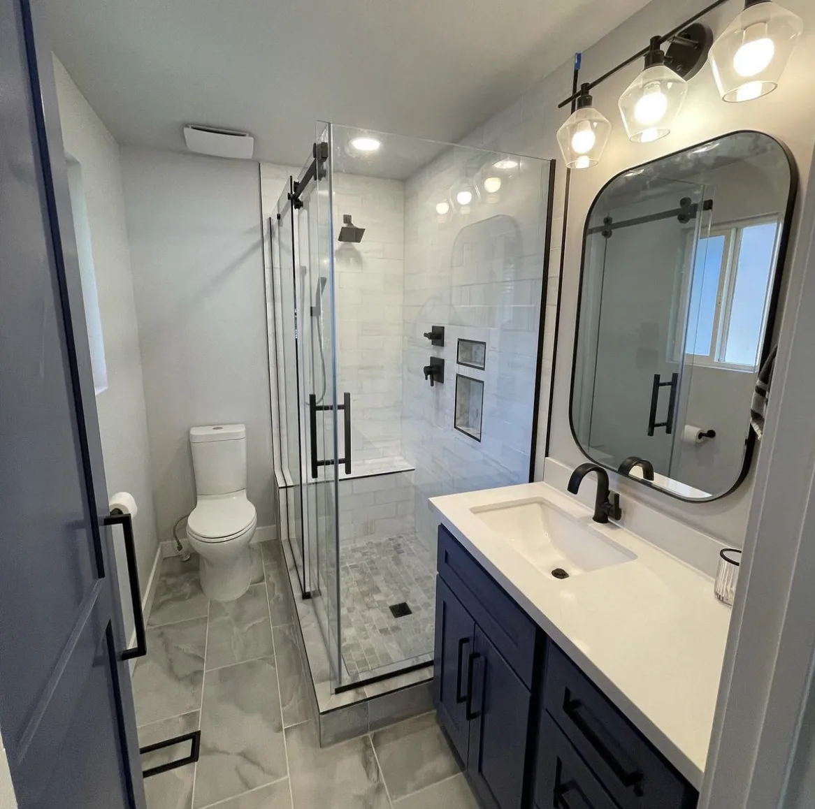 After — bathroom remodel in Utah, from a yellow bathroom with a framed corner shower to a navy vanity and frameless sliding glass shower