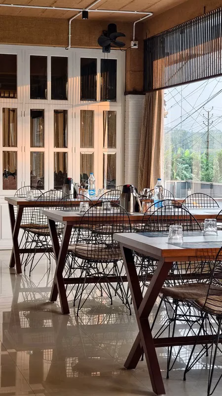 Restaurant dining area with wooden tables, wire-frame chairs, and natural lighting